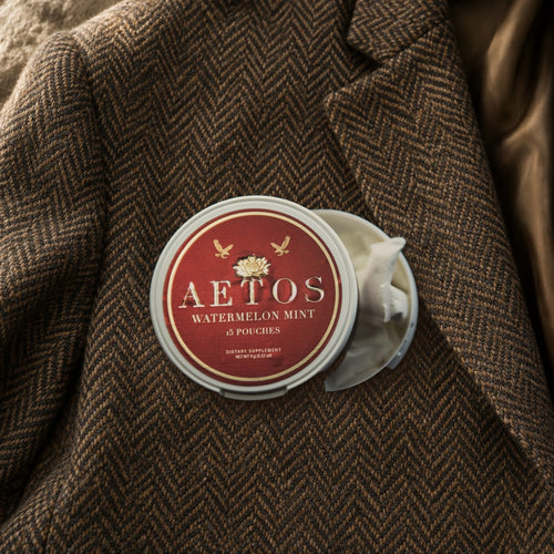 Open AETOS Watermelon Mint can on a herringbone tweed jacket